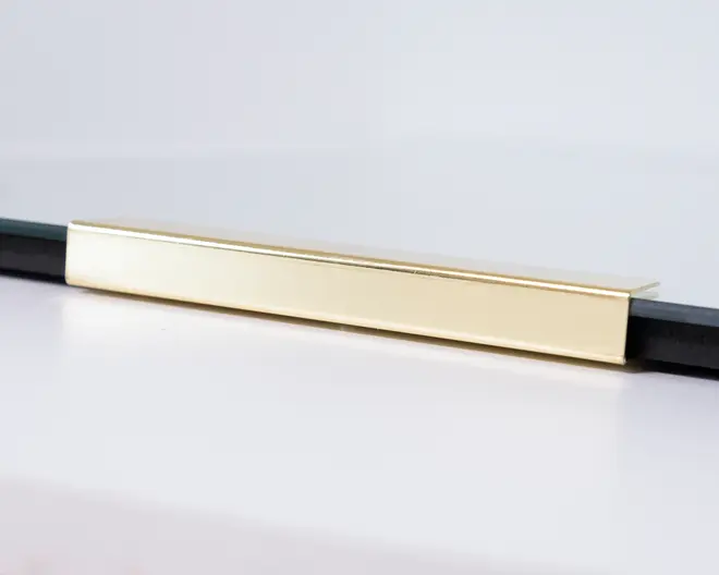 Rektangulært, moderne greb til skuffe eller skab med en glat, børstet guldfinish. Grebet har rene, lige kanter og et minimalistisk design, der passer til moderne møbler. Det er monteret vandret og ser ud til at være lavet af metal.