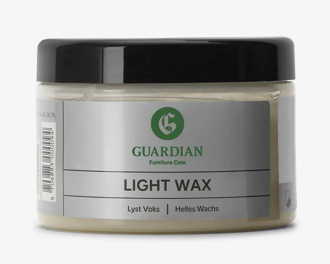 En rund, klar plastbeholder med sort skruelåg, indeholdende en lysfarvet voks. Forsiden har et sølvfarvet mærkat med grøn og sort tekst, hvor mærket 'Guardian Furniture Care' og produktnavnet 'Light Wax' fremgår. Etiketten indeholder også oversættelser på dansk og tysk samt et lille dråbeikon på siden, der indikerer voksindholdet.