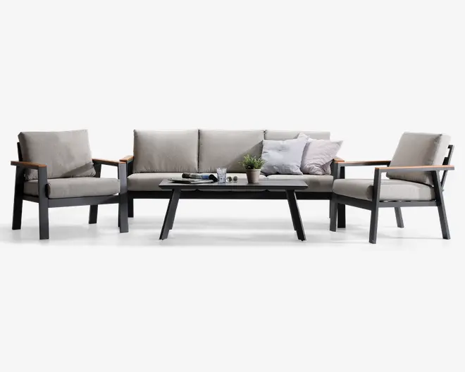 Moderne sofasæt bestående af en trepersoners sofa og to lænestole med lyse beige hynder og mørkegrå metalstel. Armlænene har trædetaljer, som giver et varmt udtryk. Sættet inkluderer et rektangulært sofabord med matchende mørkegråt stel og lys bordplade. Sofaen er pyntet med puder i neutrale og lyse nuancer, og bordet er dekoreret med en lille potteplante, et glas og en bog, hvilket skaber en hyggelig og indbydende stemning.