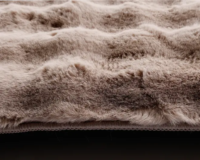 Nærbillede af et tykt, blødt stof med en fløjlsagtig overflade. Materialet har en bølget, let ujævn struktur, og fibrene fremstår tætte og fyldige, hvilket giver et luksuriøst og hyggeligt udtryk. Farven er en blanding af lyse og mellembrune beige nuancer, som giver et naturligt og varmt look.