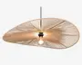 Loftlampe med en stor, asymmetrisk skærm formet som en skive, lavet af tæt vævede naturfibre, der danner et solstrålemønster. Skærmen har et åbent center, hvor pæren er synlig, hvilket giver direkte belysning. Lampen hænger i en sort ledning og har et minimalistisk, moderne udtryk med en varm, organisk tekstur.