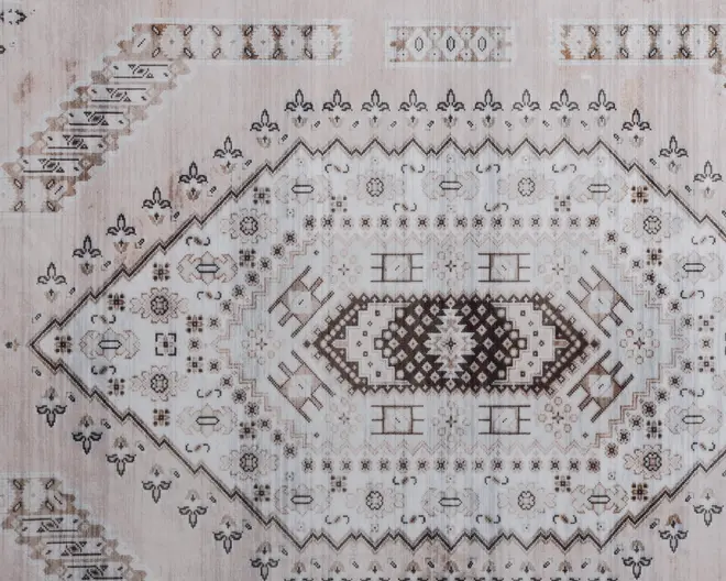 Har et centralt diamantformet midterfelt med indviklede geometriske og blomstrede motiver i nuancer af beige, brun og creme. Mønstret inkluderer symmetriske kanter og fine detaljer, hvilket giver et vintage og let slidt udtryk. Overfladen ser blød ud med en let falmet finish, der understreger det antikke look.