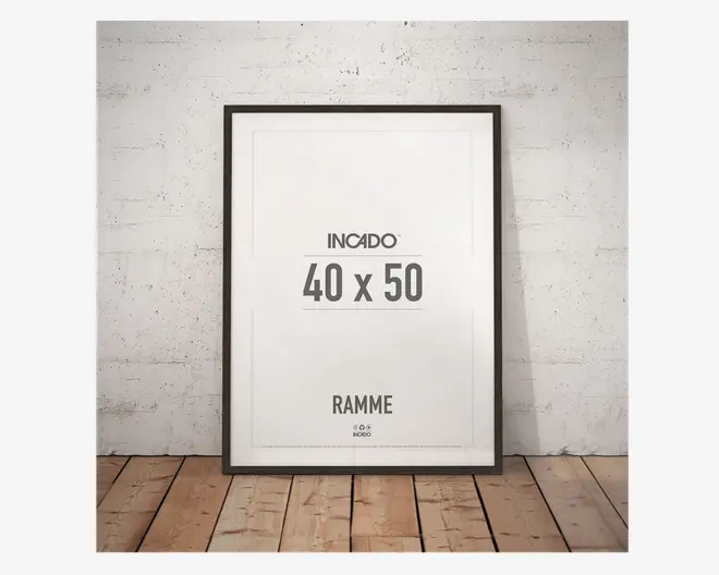 En rektangulær ramme med en tynd, sort kant, der passer til et billede på 40 x 50 cm. Rammen har et moderne, minimalistisk design og står op ad en hvid, tekstureret væg på et trægulv. Fronten er klar glas eller akryl, og rammen har en glat, mat overflade.