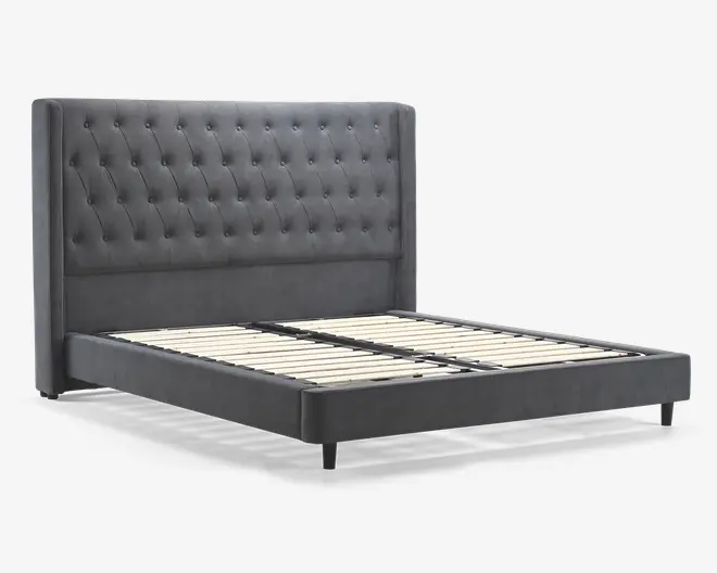 Denne sengeramme har en høj, polstret sengegavl med dybe knap-tuftede detaljer for et klassisk og elegant udtryk. Sengegavlen har vingeformede sider, som giver et sofistikeret præg og ekstra støtte. Rammen er betrukket med et blødt, mørkegråt stof, og bunden har solide lameller i træ til at støtte madrassen, så en boxmadras ikke er nødvendig. Benene er korte og cylindriske, hvilket giver stabilitet og et moderne udtryk.