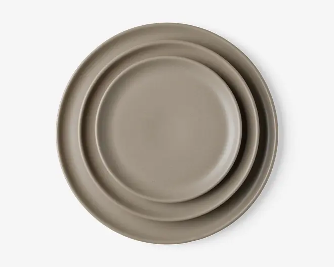 Sæt med tre runde tallerkener i forskellige størrelser, alle i en mat taupe-farve. Tallerkenerne har en glat, enkel overflade og en let forhøjet kant, hvilket giver et minimalistisk og moderne udtryk.