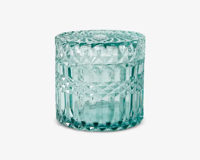 Rund, gennemsigtig glaskrukke med tilhørende låg, dekoreret med et detaljeret diamantmønster på siderne og toppen. Glasset har et let blågrønt skær, hvilket giver et vintage eller dekorativt udtryk. Låget slutter tæt, og det samlede design reflekterer lyset og skaber en funklende effekt.