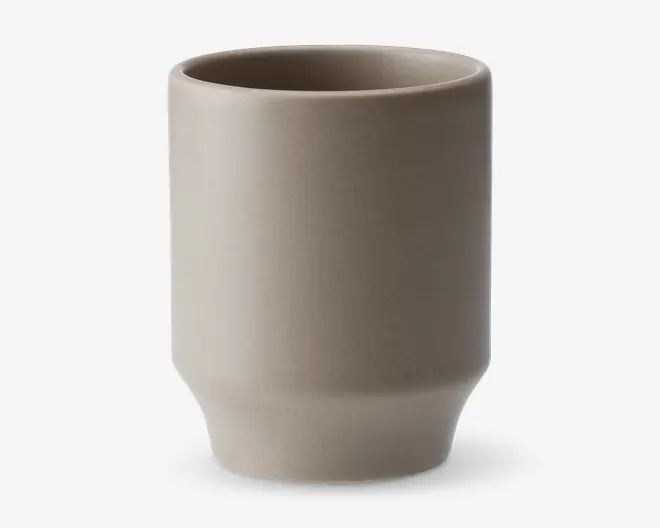 En minimalistisk, cylindrisk kop med mat beige overflade. Koppen har lige sider og en let tilspidset bund, hvilket giver et moderne og enkelt udtryk. Randen er glat, og overfladen er uden dekoration, hvilket fremhæver det enkle design.