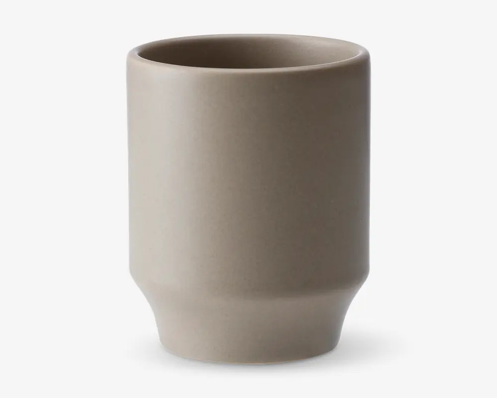 En minimalistisk, cylindrisk kop med mat beige overflade. Koppen har lige sider og en let tilspidset bund, hvilket giver et moderne og enkelt udtryk. Randen er glat, og overfladen er uden dekoration, hvilket fremhæver det enkle design.