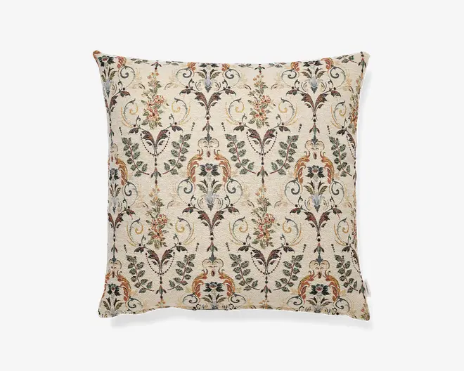 Firkantet pyntepude med cremefarvet baggrund og et detaljeret gentaget mønster med blomster og paisley i afdæmpede grønne, bordeaux, gyldne og brune nuancer.