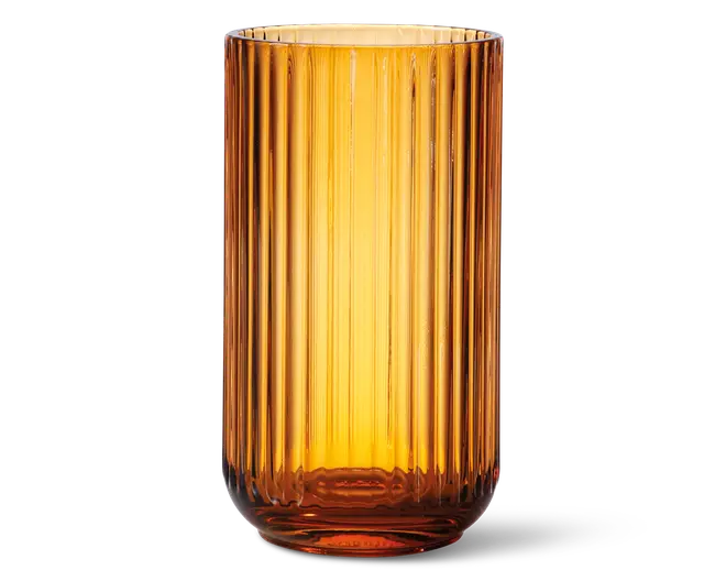 Høj, cylindrisk beholder lavet af ravfarvet glas med lodret rillet struktur. Glasset er gennemsigtigt, hvilket lader lyset skinne igennem og fremhæver den varme, gyldne farve. Kanten er glat, og bunden er en smule tykkere for ekstra stabilitet.