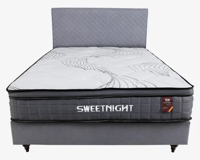 En enkeltseng med en tyk, quiltet madras, der har en hvid top med diskrete grå bølgemønstre. Madrassen har en grå side med ternet mønster og mærket 'SWEETNIGHT' broderet med hvidt. Sengen har et matchende gråt hovedgærde med diamantmønster og en solid grå bund med korte ben.