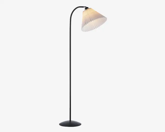 Høj gulvlampe med en slank, buet metalstang i kromfinish, rund sort fod for stabilitet og en plisseret hvid lampeskærm, der spreder lyset blødt nedad.