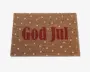 Rektangulært dørmåtte med naturlig kokosfiberstruktur, hvor teksten 'God Jul' står med store røde bogstaver i midten. Overfladen er dekoreret med jævnt fordelte hvide prikker, hvilket giver et festligt og julet udtryk.