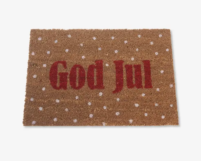 Rektangulært dørmåtte med naturlig kokosfiberstruktur, hvor teksten 'God Jul' står med store røde bogstaver i midten. Overfladen er dekoreret med jævnt fordelte hvide prikker, hvilket giver et festligt og julet udtryk.