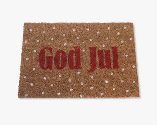 Rektangulært dørmåtte med naturlig kokosfiberstruktur, hvor teksten 'God Jul' står med store røde bogstaver i midten. Overfladen er dekoreret med jævnt fordelte hvide prikker, hvilket giver et festligt og julet udtryk.