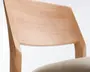 Nærbillede af en stol med buet ryglæn i lyst træ med glat overflade og kantede kanter. Sædet er polstret med et lyst beige stof, som giver en blød kontrast til det naturlige træ. Designet fremhæver rene linjer og et minimalistisk udtryk.