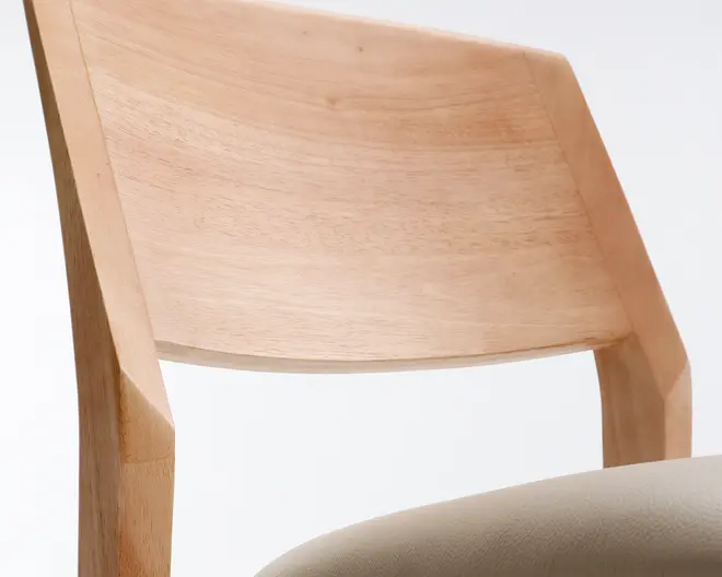 Nærbillede af en stol med buet ryglæn i lyst træ med glat overflade og kantede kanter. Sædet er polstret med et lyst beige stof, som giver en blød kontrast til det naturlige træ. Designet fremhæver rene linjer og et minimalistisk udtryk.