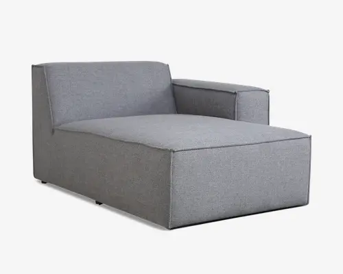 Moderne chaiselong betrukket med lysegråt stof, med en bred og dyb siddeflade for ekstra komfort. Designet har én armlæn på højre side og et lavt, lige ryglæn, begge med rene, skarpe linjer. Betrækket er glat og stramt, hvilket giver møblet et stilrent og moderne udtryk. Basen er solid og firkantet uden synlige ben, hvilket understreger det minimalistiske design.