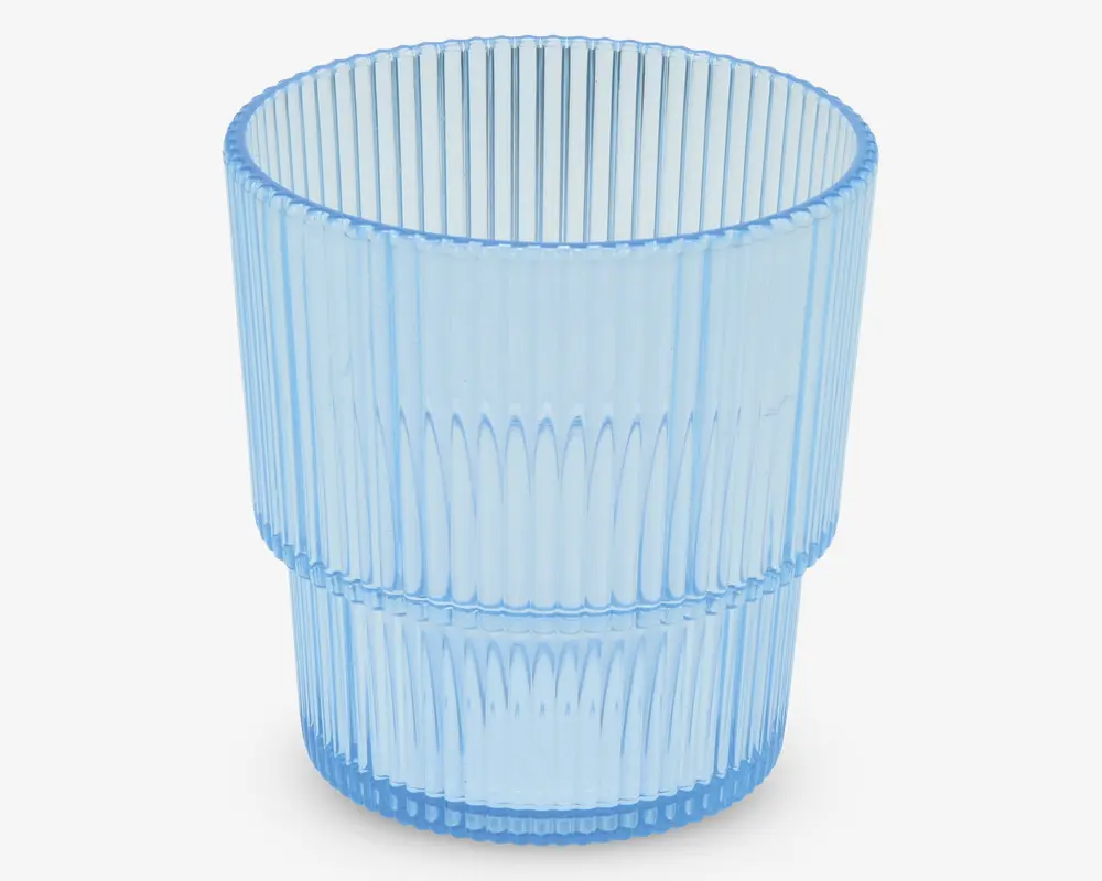 Et transparent lyseblåt drikkeglas med cylindrisk form. Overfladen har lodrette rillede linjer, som giver et tekstureret greb, og glasset er delt i to sektioner af en diskret vandret kant omkring midten. Designet er moderne og elegant, velegnet til servering af kolde drikke.