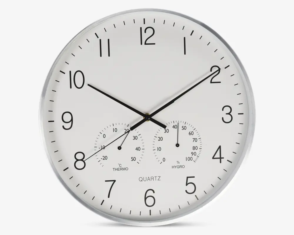 Rund vægur med hvid urskive og sorte tal, udstyret med tre sorte visere til timer, minutter og sekunder. Uret har også to små målere nederst: én til temperatur (termometer) og én til luftfugtighed (hygrometer), begge med tydelige markeringer og sorte visere. Rammen er sølvfarvet, og designet er minimalistisk og let at aflæse.