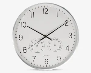 Rund vægur med hvid urskive og sorte tal, udstyret med tre sorte visere til timer, minutter og sekunder. Uret har også to små målere nederst: én til temperatur (termometer) og én til luftfugtighed (hygrometer), begge med tydelige markeringer og sorte visere. Rammen er sølvfarvet, og designet er minimalistisk og let at aflæse.