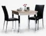 Et kompakt spisesæt bestående af et kvadratisk bord i lyst træ med slanke kromben og to matchende stole. Stolene har sort kunstlæderpolstring med vandrette syninger og kromben. Bordet er dækket med en skål, en kop, en tallerken, en vase med lyserøde blomster og et dekorativt lys, hvilket giver et moderne og indbydende udtryk, der passer til små rum.