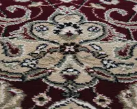 Nærbillede af en blød, tekstureret overflade med et udsmykket blomstermønster og slyngede ranker i beige, creme og sort på en dyb rød baggrund. Designet er symmetrisk og detaljeret med fine konturer og diskrete farvevariationer, hvilket giver et klassisk og elegant udtryk.