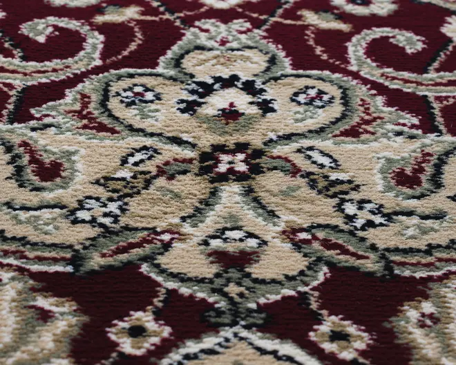 Nærbillede af en blød, tekstureret overflade med et udsmykket blomstermønster og slyngede ranker i beige, creme og sort på en dyb rød baggrund. Designet er symmetrisk og detaljeret med fine konturer og diskrete farvevariationer, hvilket giver et klassisk og elegant udtryk.