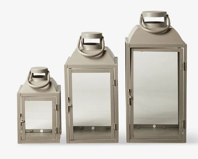 Sæt med tre lanterner i forskellige størrelser, hver med en rektangulær form, flad bund og glasfrontdør. Lanterne har en mat beige finish og et robust metalhåndtag øverst til nem transport eller ophængning. Dørene lukkes med en lås, og designet er enkelt og moderne, velegnet til både indendørs og udendørs brug.