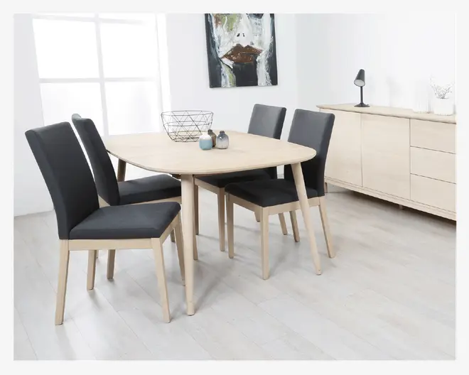 Et moderne spisebordssæt med et ovalt bord i lyst træ med afrundede kanter og fire matchende stole. Stolene har stel og ben i lyst træ samt mørkegrå polstrede sæder og rygge, hvilket giver en flot kontrast. Bordpladen er glat og enkel, kun dekoreret med en trådkurv og et par små pyntegenstande. Designet er minimalistisk og nutidigt med rene linjer og neutrale farver.