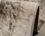 Nærbillede af et tæppe med en blød, plysset overflade og et moderne abstrakt mønster i nuancer af creme, grå og diskrete strejf af brun. Kanterne er pænt afsluttet med en slidstærk kant, og tæppet fremstår tykt og velpolstret, hvilket giver god komfort under fødderne. Undersiden har en tæt vævet bagside for ekstra holdbarhed og stabilitet på gulvet.