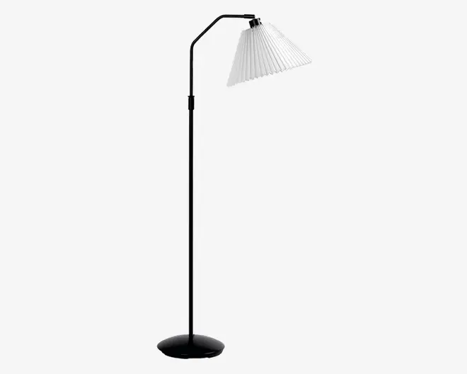 Høj gulvlampe med en slank, sort metalstang og en rund, stabil fod. Lampen har en vinklet arm øverst, der holder en hvid, plisseret lampeskærm, som leder lyset nedad. Designet er moderne og minimalistisk, velegnet til læsning eller stemningsbelysning.