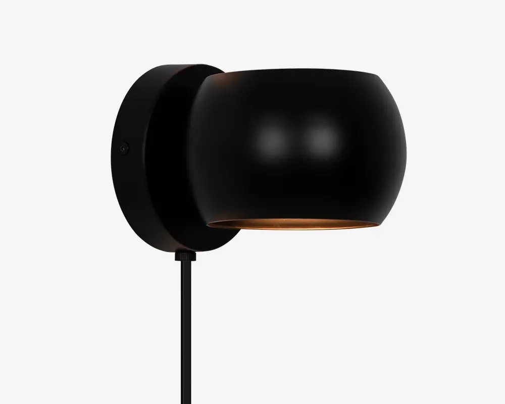 Væghængt armatur i mat sort med en rund, skålformet skærm. Skærmen leder lyset nedad og giver en fokuseret belysning. Armaturet har et minimalistisk design med en glat overflade og skjult monteringsplade, hvilket giver et moderne og stilrent udtryk.