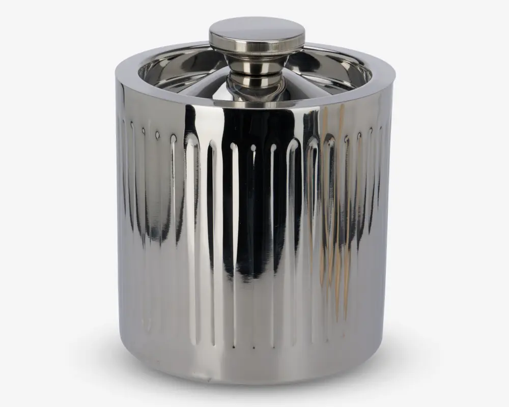 En cylindrisk beholder i poleret rustfrit stål med tilhørende låg. Ydersiden har lodrette, jævnt fordelte riller, der giver et tekstureret udseende. Låget har et rundt, fladt håndtag, som gør det nemt at løfte. Det samlede design er moderne og reflekterende, hvilket giver et stilrent og elegant udtryk.