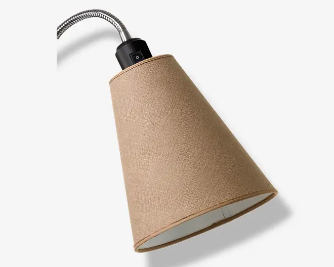 Billedet viser en konisk lampeskærm betrukket med et tekstureret, lysebrunt stof. Lampeskærmen er monteret på en fleksibel, metalbøjelige arm, som gør det muligt at justere positionen. Øverst er der en sort plastikfatning med en synlig tænd/sluk-knap for nem betjening. Indersiden af skærmen er hvid, hvilket hjælper med at reflektere lyset effektivt.