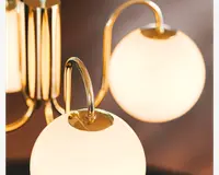 Nærbillede af en moderne lampe med kugleformede, matglas skærme og polerede guldfarvede metalarme. Designet fremhæver bløde kurver og en luksuriøs finish, hvor gulddetaljerne giver en elegant kontrast til det bløde, diffuse lys fra glasskærmene.