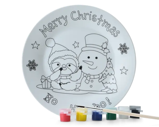Rund hvid tallerken med et sort konturjulemotiv, der viser en pingvin i nissehue ved siden af en snemand, med stjerner, snefnug, et lille juletræ og teksten "Merry Christmas" øverst. Små malerbøtter og en pensel er vist langs nederste kant.