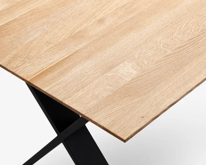 Nærbillede af en bordplade med lys egetræsfinish, der viser naturlige træmønstre. Kanten er lige og glat, og bordet understøttes af en sort metalramme med et moderne, vinklet design.