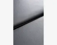 Nærbillede af en mørkegrå overflade med en subtil kornet struktur, hvor to paneler mødes ved en synlig samling. Materialet ligner syntetisk læder eller lignende, med en mat finish og ensartet, fin tekstur.