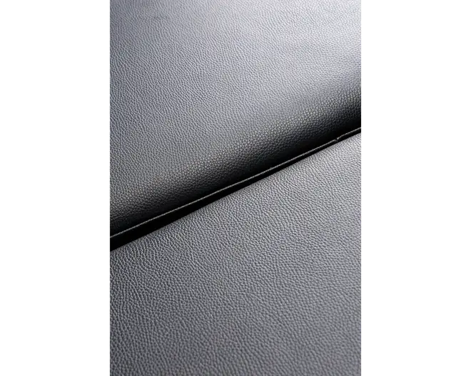 Nærbillede af en mørkegrå overflade med en subtil kornet struktur, hvor to paneler mødes ved en synlig samling. Materialet ligner syntetisk læder eller lignende, med en mat finish og ensartet, fin tekstur.