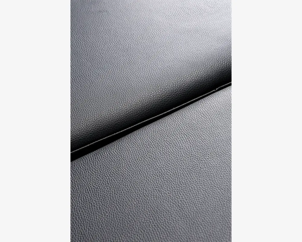 Nærbillede af en mørkegrå overflade med en subtil kornet struktur, hvor to paneler mødes ved en synlig samling. Materialet ligner syntetisk læder eller lignende, med en mat finish og ensartet, fin tekstur.