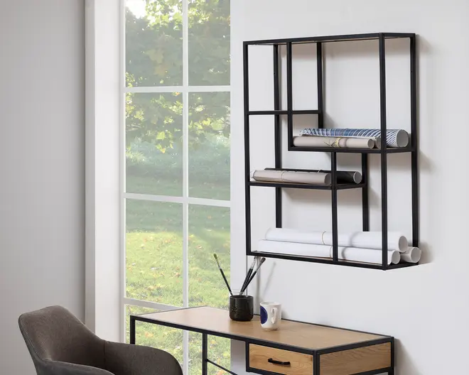 Et moderne, geometrisk vægmonteret reolsystem lavet af sort metal med flere rektangulære rum i forskellige størrelser. Hylderne bruges til opbevaring af sammenrullede papirer og tegninger. Enheden har et minimalistisk, åbent design og er monteret over et skrivebord i træ med sorte metalben. Det samlede udtryk er moderne og funktionelt, velegnet til et kontor eller et kreativt arbejdsområde.