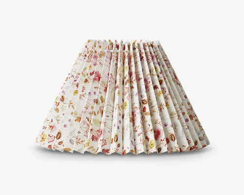 Plisseret lampeskærm med bred, udvidet form. Stoffet har et fint blomstermønster i nuancer af pink, rød, gul og grøn på hvid baggrund. Plisseringerne giver et tekstureret, struktureret udtryk, og det blomstrede design tilføjer et blødt, dekorativt præg.