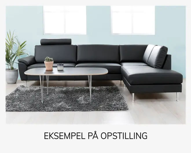 Moderne L-formet sofa med sort læderbetræk, rene linjer og lav ryg, hvoraf den ene ende har et justerbart hovedstøtte. Sofaen har metalben, fast og rummelig siddeplads samt en chaiselong til højre. Den står på et lyst trægulv med et gråt, blødt tæppe under og et minimalistisk ovalt sofabord med tynde metalben foran. Bordet er pyntet med en potteplante og et lille lys.