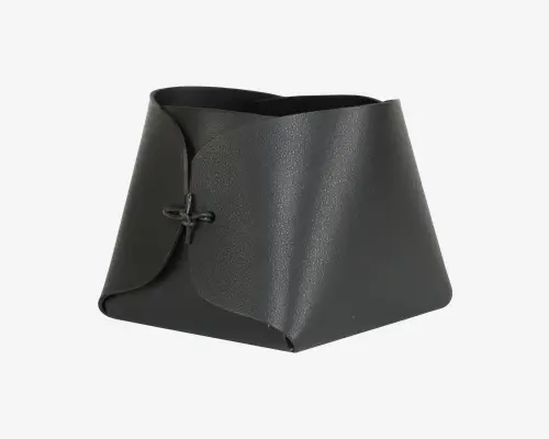 En sort, tekstureret, trapezformet beholder lavet af et enkelt stykke materiale, der er foldet og samlet foran med en simpel knude. Kanterne er glatte, og strukturen er robust med et moderne, minimalistisk design. Åbningen foroven er bred, hvilket gør det nemt at få adgang til indholdet.