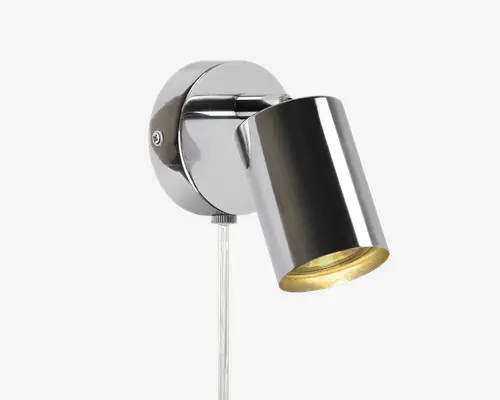 Væghængt spotlampe med blank kromfinish, der har et cylindrisk, justerbart lampehoved til retningsbestemt belysning. Lampen har en rund base og en synlig ledning, der går nedad. Indersiden af lampehovedet er gylden, hvilket giver et varmt lys.