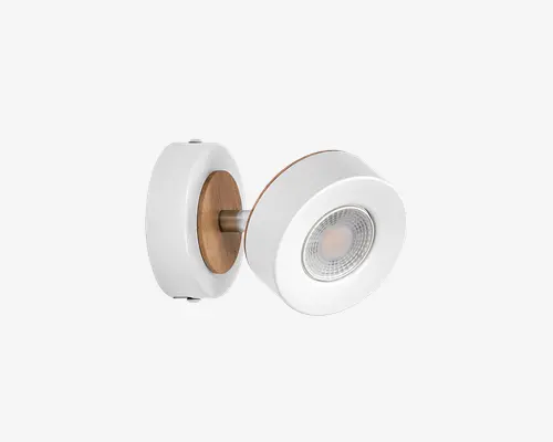 Moderne vægmonteret lampe med et cirkulært design og mat hvid finish. Både basen og lampehuset har trædetaljer, som giver et varmt præg til det moderne udtryk. Lyskilden er forsænket og dækket af en klar linse, hvilket giver fokuseret belysning. Lampen er monteret på væggen med en kort metalarm.