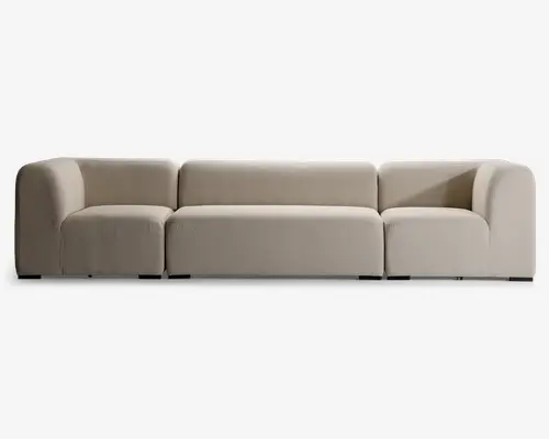 Moderne, modulopbygget sofa med lav profil og bløde, afrundede armlæn. Polstret i et lysebeige stof med en blød, tekstureret overflade. Sofaen har tre separate siddepladser med brede og dybe sæder for ekstra komfort. Udtrykket er minimalistisk og nutidigt, hvilket gør den velegnet til mange forskellige stuer.