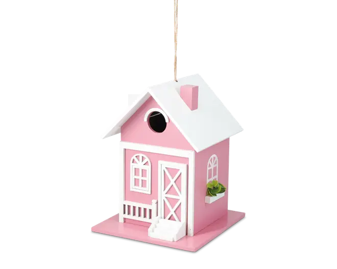 Et lille, dekorativt husformet objekt malet lyserødt med hvide kanter. Det har et saddeltag med skorsten, en lille veranda med gelænder, en hvid dør med krydsmønster og buede vinduer. Der er en cirkulær åbning over døren, og en miniature blomsterkasse med grønne planter er fastgjort under et af sidevinduerne. Objektet hænger i en snor, der er fastgjort til taget.