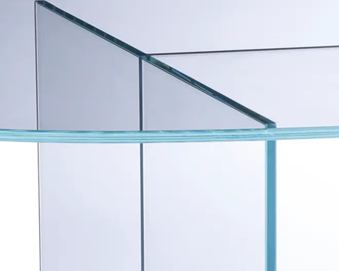 Nærbillede af en gennemsigtig glasstruktur med rene, skarpe kanter og glatte overflader. Glaspladerne er samlet uden synlige samlinger, og hjørnerne er forstærket for stabilitet. Glasset har en let blålig nuance langs kanterne, hvilket indikerer tykkelse og kvalitet. Det overordnede design er moderne og minimalistisk.